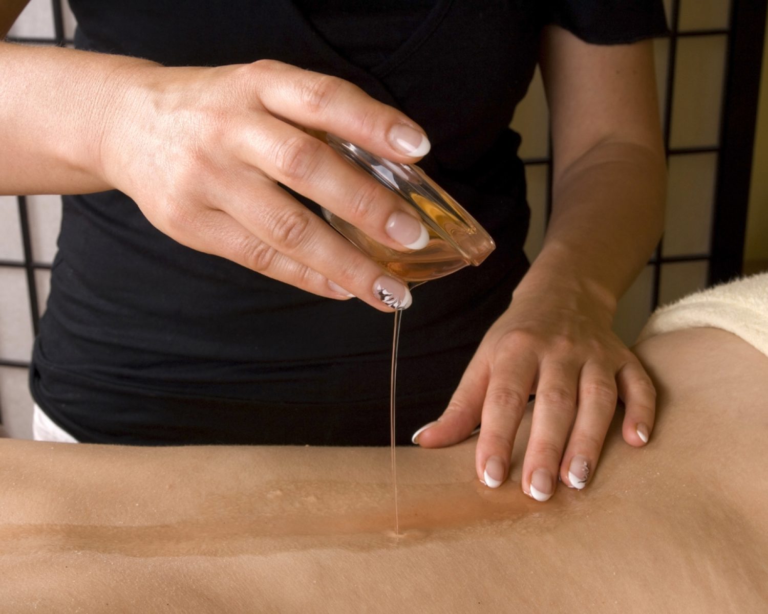Preparing for relax massage inside a spa room, hands putting the the warm oil from a bowl on the back as a closeup image