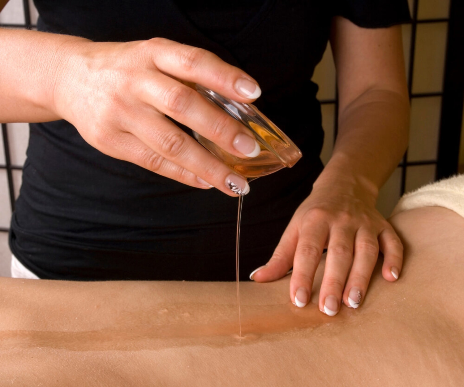 Preparing for relax massage inside a spa room, hands putting the the warm oil from a bowl on the back as a closeup image